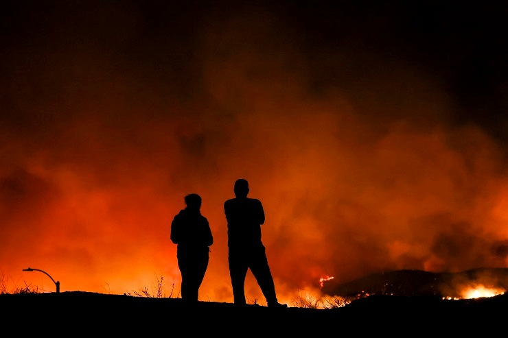 Due persone osservano i tentativi dei vigili del fuoco di domare l'incendio